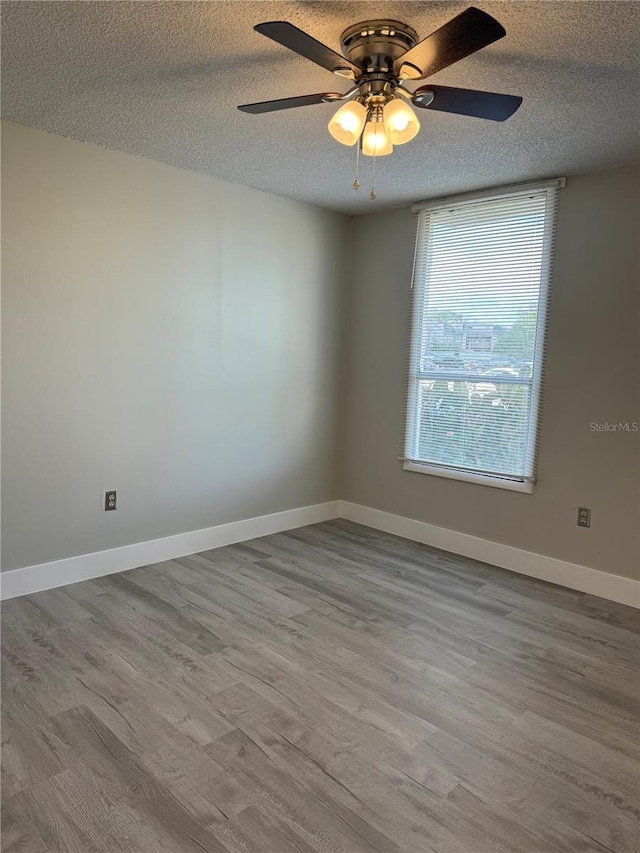 empty room with a textured ceiling, baseboards, and wood finished floors