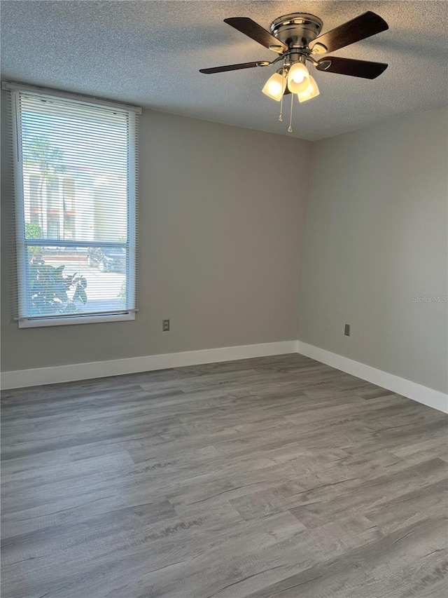 empty room with ceiling fan, wood finished floors, baseboards, and a textured ceiling