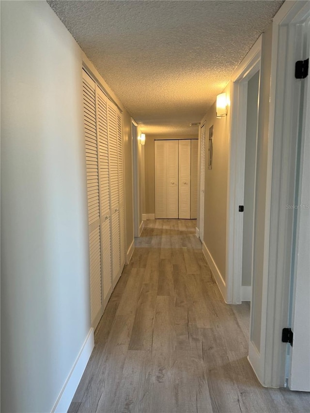 hall featuring a textured ceiling, baseboards, and wood finished floors