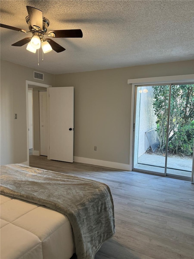 bedroom featuring access to exterior, visible vents, baseboards, wood finished floors, and a textured ceiling