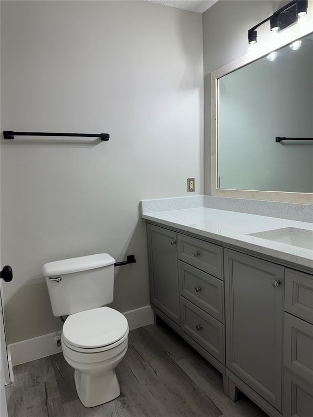 half bath with baseboards, toilet, wood finished floors, and vanity