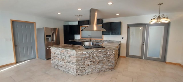 kitchen featuring wall chimney exhaust hood, hanging light fixtures, stainless steel fridge, sink, and a notable chandelier