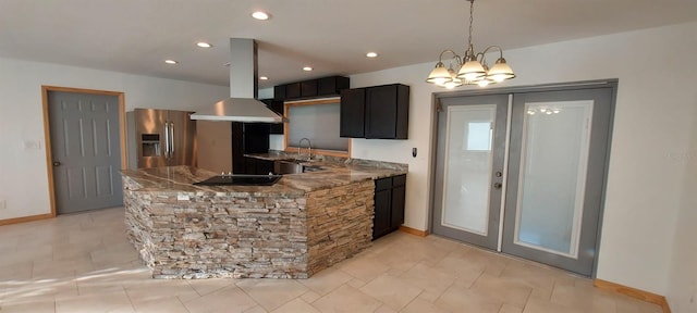 kitchen with an inviting chandelier, sink, range hood, stainless steel refrigerator with ice dispenser, and light stone counters