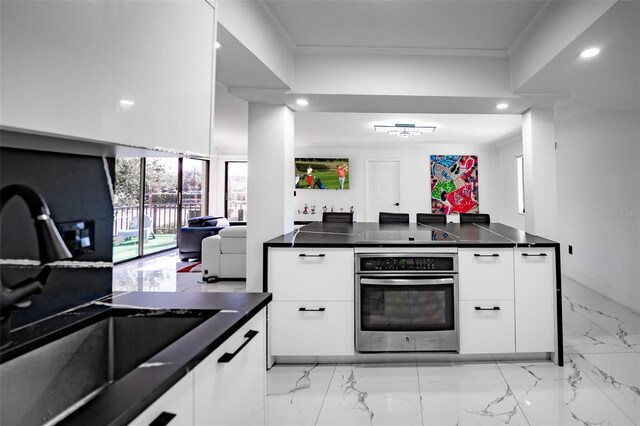 kitchen with ornamental molding, dark countertops, white cabinets, and stainless steel oven