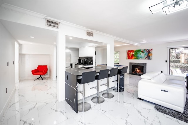 kitchen with a lit fireplace, ornamental molding, visible vents, and white cabinets