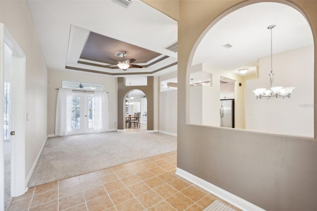 entrance foyer with french doors, light carpet, ceiling fan with notable chandelier, and a raised ceiling