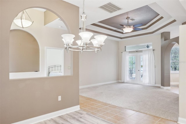 spare room featuring ceiling fan with notable chandelier, french doors, a tray ceiling, light carpet, and ornamental molding