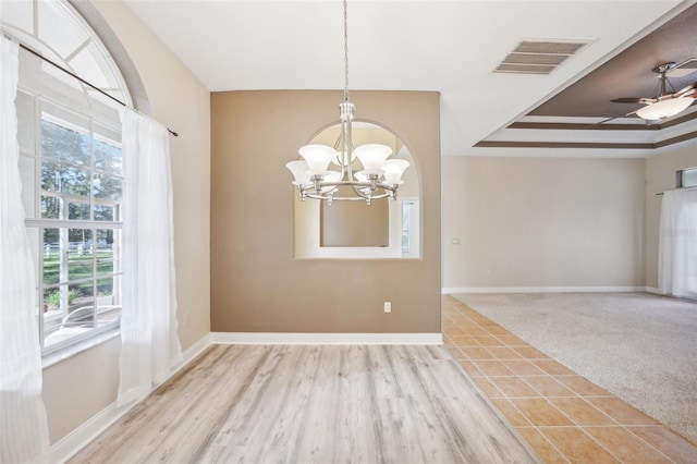 unfurnished dining area featuring light hardwood / wood-style floors, ceiling fan with notable chandelier, and a raised ceiling