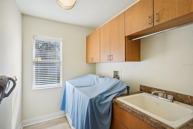 laundry room featuring hookup for a washing machine, sink, cabinets, a textured ceiling, and light hardwood / wood-style floors