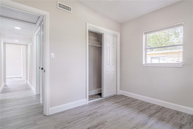 unfurnished bedroom featuring light wood-type flooring, a textured ceiling, and a closet