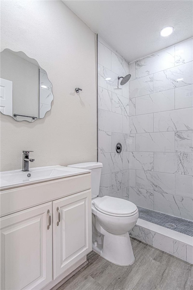 bathroom featuring hardwood / wood-style floors, vanity, toilet, and tiled shower