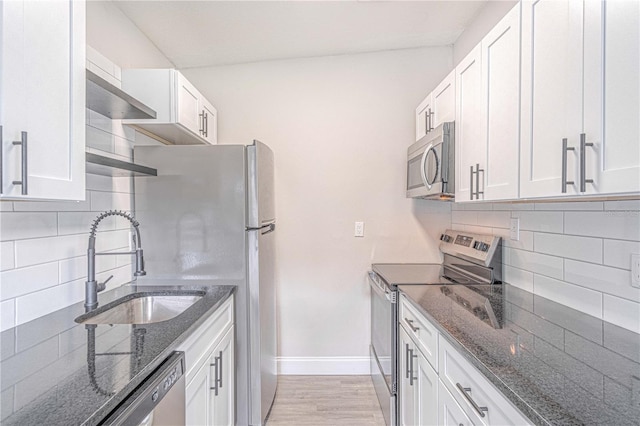 kitchen featuring stainless steel appliances, light hardwood / wood-style floors, dark stone counters, white cabinets, and decorative backsplash