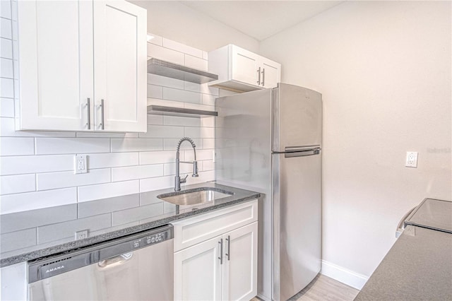 kitchen with tasteful backsplash, stainless steel appliances, sink, white cabinets, and light hardwood / wood-style flooring