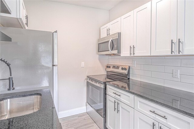 kitchen featuring stainless steel appliances, white cabinetry, sink, tasteful backsplash, and dark stone counters