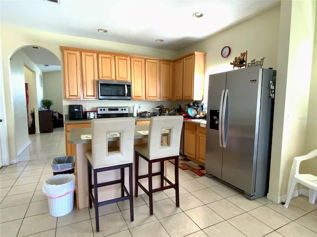 kitchen featuring appliances with stainless steel finishes, light tile patterned floors, a kitchen bar, and a kitchen island