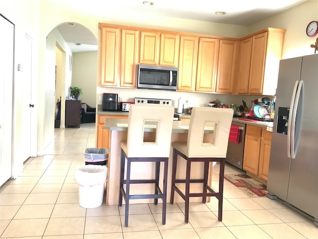 kitchen featuring light brown cabinets, light tile patterned floors, appliances with stainless steel finishes, a kitchen bar, and a center island