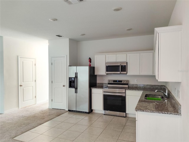 kitchen featuring sink, white cabinetry, stainless steel appliances, dark stone countertops, and light colored carpet