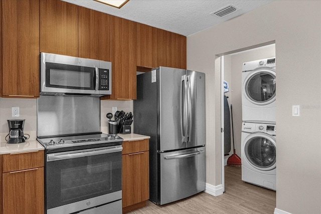 kitchen featuring stacked washer / dryer, a textured ceiling, appliances with stainless steel finishes, and light hardwood / wood-style flooring