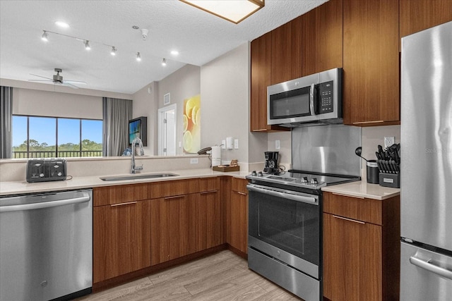 kitchen featuring appliances with stainless steel finishes, sink, light wood-type flooring, a textured ceiling, and ceiling fan