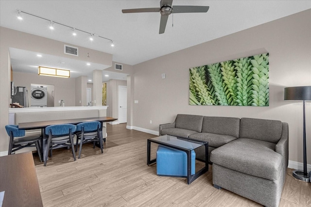 living room with light hardwood / wood-style flooring, stacked washer and clothes dryer, and ceiling fan