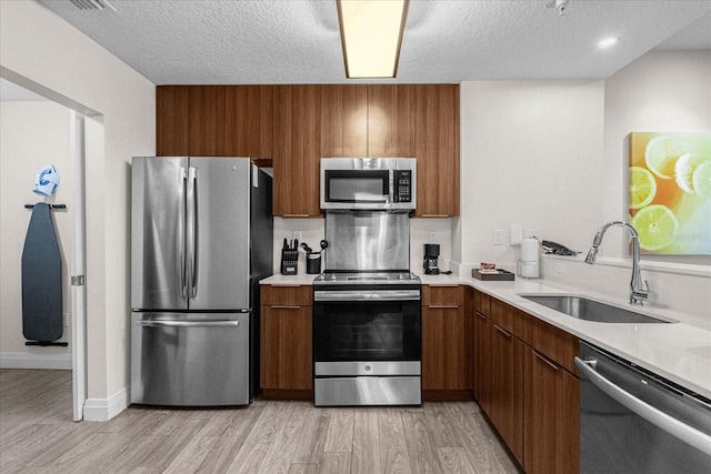 kitchen featuring sink, appliances with stainless steel finishes, a textured ceiling, and light hardwood / wood-style floors