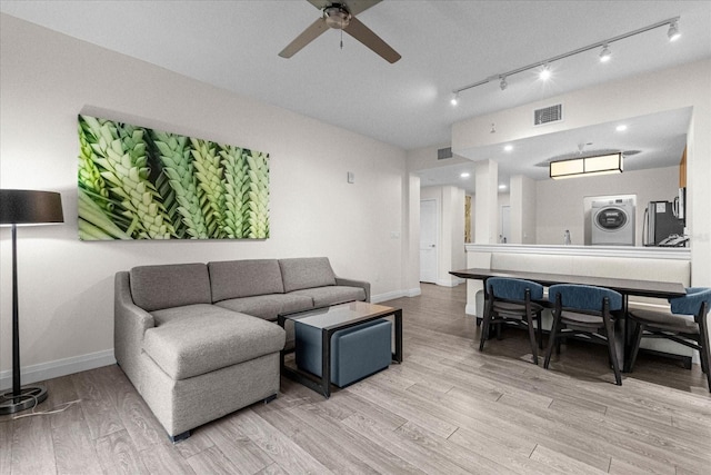 living room with stacked washer / drying machine, rail lighting, light wood-type flooring, and ceiling fan