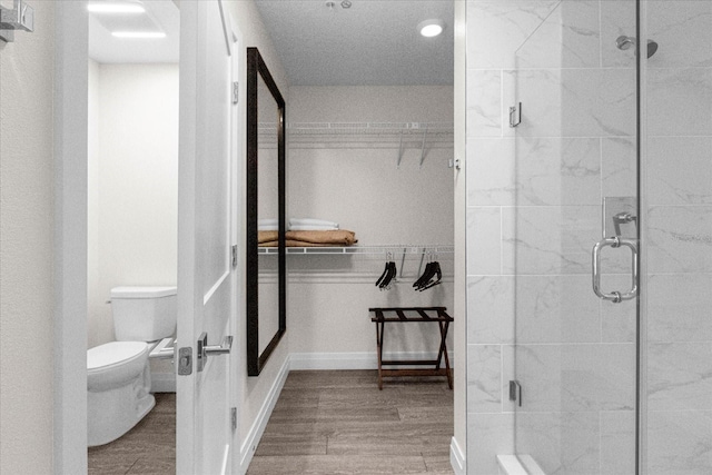 bathroom featuring toilet, a shower with shower door, and wood-type flooring