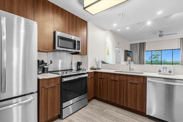 kitchen with light hardwood / wood-style floors, a textured ceiling, appliances with stainless steel finishes, and sink