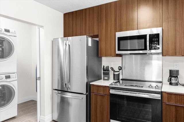 kitchen featuring stacked washing maching and dryer, appliances with stainless steel finishes, a textured ceiling, and light wood-type flooring