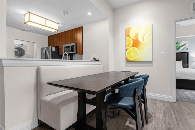 dining space with stacked washer / drying machine, a textured ceiling, and light wood-type flooring