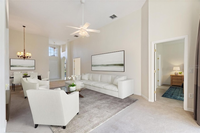 living room with a towering ceiling, light carpet, and ceiling fan with notable chandelier