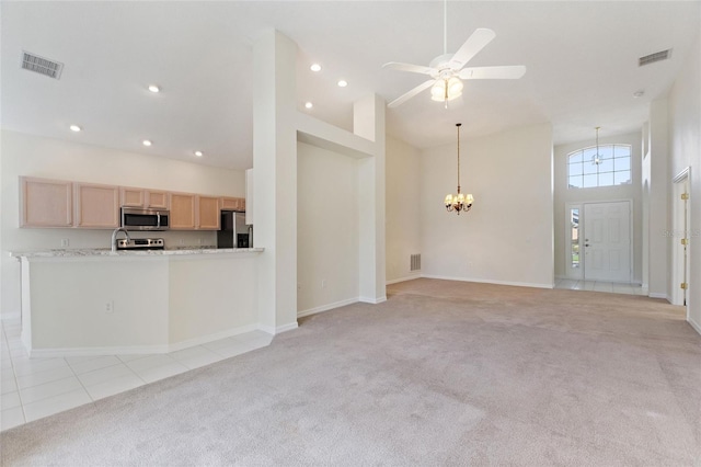 unfurnished living room featuring light carpet, sink, ceiling fan with notable chandelier, and a high ceiling