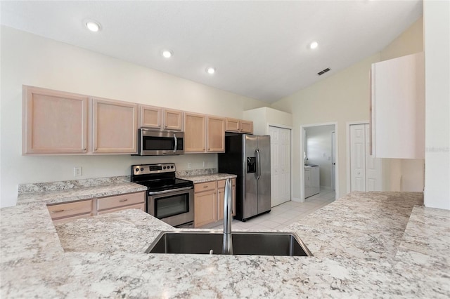 kitchen with light brown cabinets, stainless steel appliances, sink, light stone countertops, and washing machine and dryer