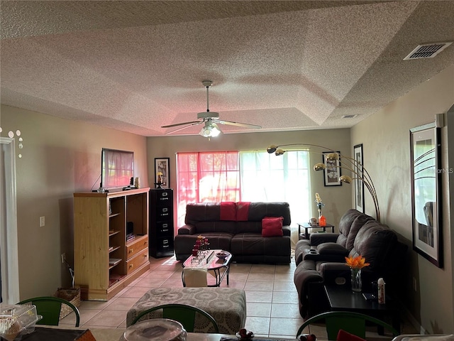 living room with a textured ceiling, light tile patterned flooring, a tray ceiling, and ceiling fan