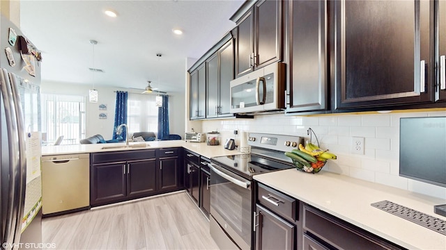 kitchen with sink, pendant lighting, light wood-type flooring, appliances with stainless steel finishes, and ceiling fan