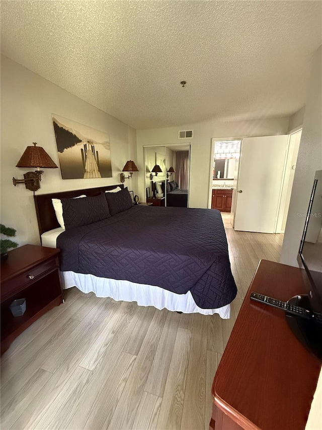 bedroom with a textured ceiling, light hardwood / wood-style floors, and ensuite bath