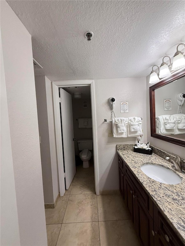 bathroom featuring vanity, a textured ceiling, toilet, and tile patterned floors