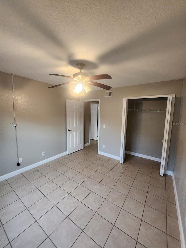 unfurnished bedroom featuring a closet, a textured ceiling, light tile patterned floors, and ceiling fan