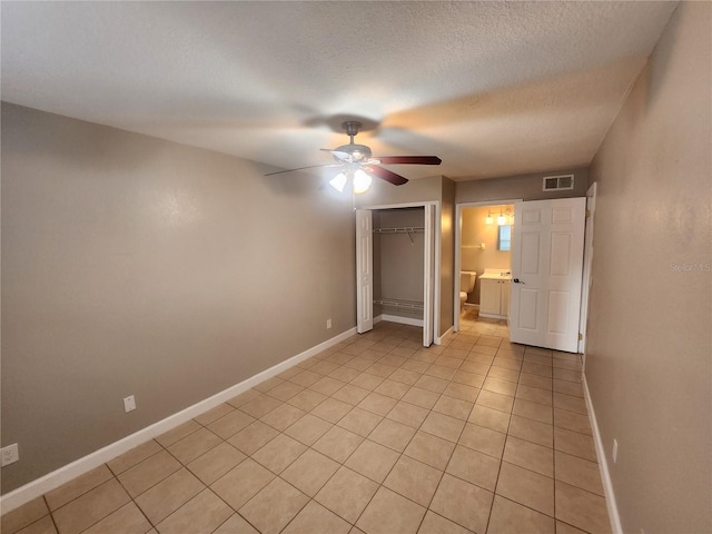 unfurnished bedroom with light tile patterned floors, ceiling fan, a textured ceiling, a closet, and ensuite bath