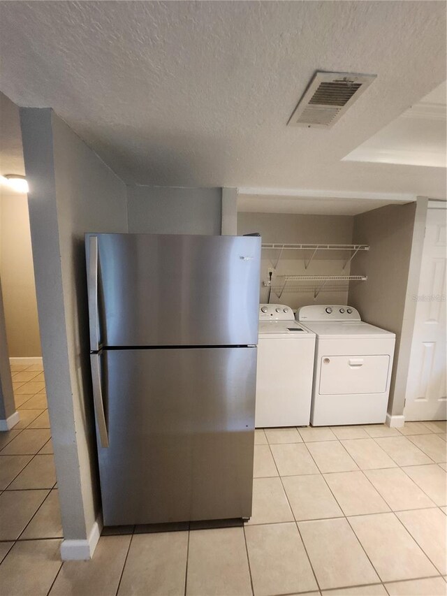 clothes washing area featuring a textured ceiling, washing machine and clothes dryer, and light tile patterned floors