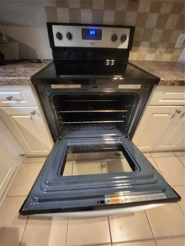 details featuring tile patterned floors, black electric range oven, and white cabinets