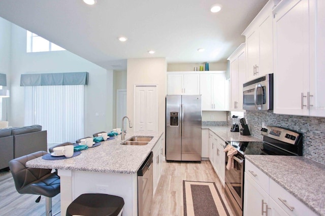 kitchen featuring white cabinetry, sink, stainless steel appliances, a breakfast bar, and a center island with sink