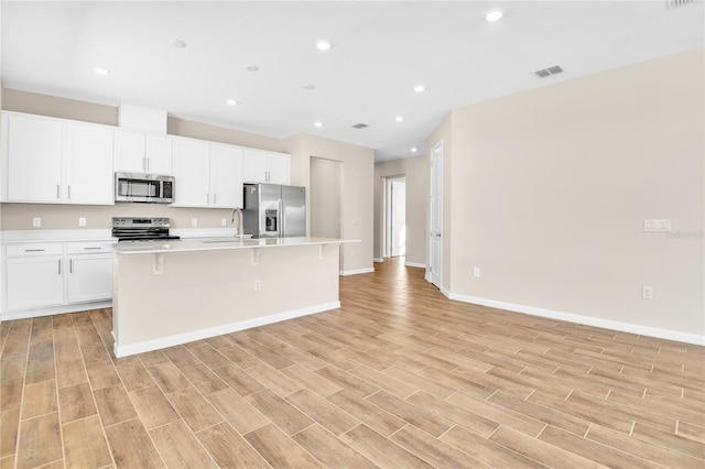 kitchen featuring sink, appliances with stainless steel finishes, white cabinets, a center island with sink, and light wood-type flooring