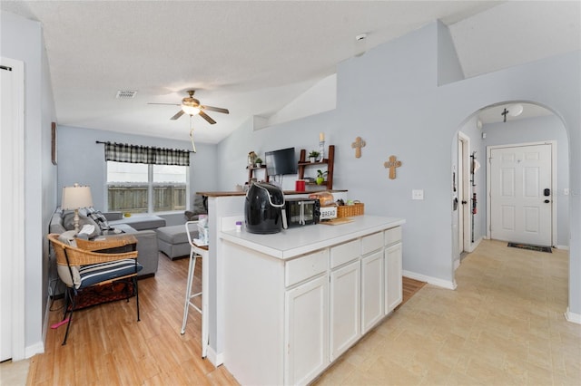 kitchen with lofted ceiling, white cabinetry, a textured ceiling, light hardwood / wood-style floors, and ceiling fan