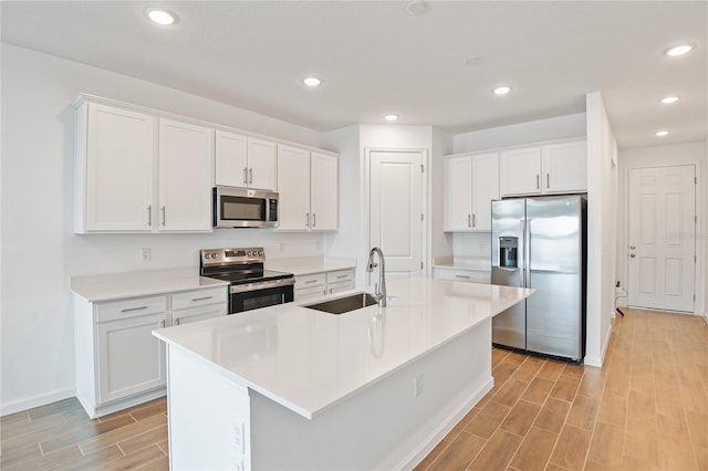 kitchen featuring white cabinetry, sink, stainless steel appliances, and an island with sink