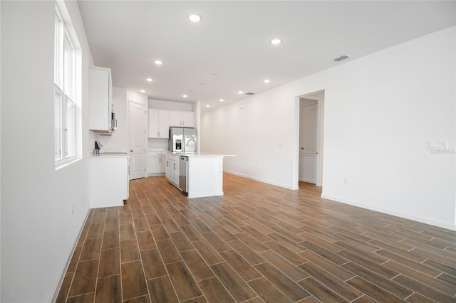 kitchen with appliances with stainless steel finishes, dark hardwood / wood-style floors, a center island with sink, and white cabinets