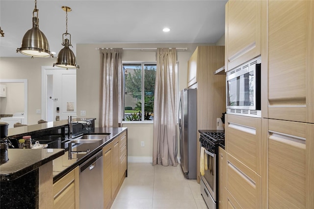 kitchen with light brown cabinets, stainless steel appliances, dark stone countertops, sink, and light tile patterned floors