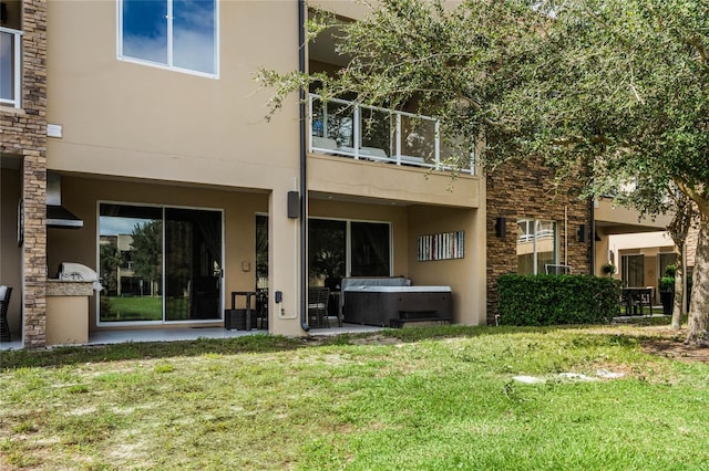 back of house with a hot tub, a lawn, and a balcony