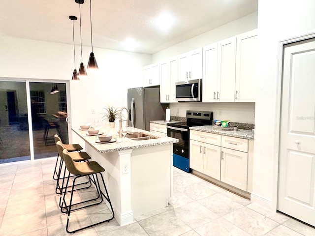 kitchen with pendant lighting, white cabinetry, a kitchen island with sink, stainless steel appliances, and light stone countertops