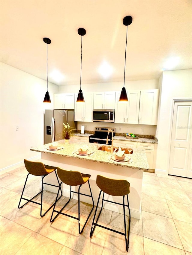 kitchen with a breakfast bar area, appliances with stainless steel finishes, a kitchen island with sink, light stone counters, and white cabinets